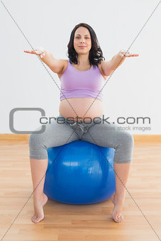 Pregnant woman sitting on blue exercise ball with arms outstretched
