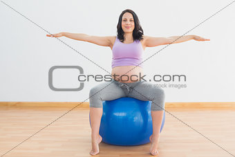 Pregnant woman sitting on blue exercise ball with arms out