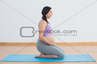 Pregnant brunette kneeling on exercise mat