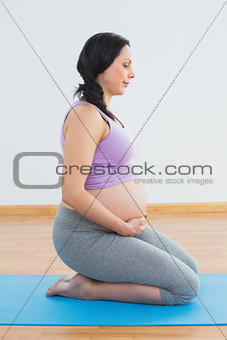 Happy pregnant brunette kneeling on exercise mat