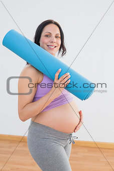 Pregnant woman holding exercise mat smiling at camera