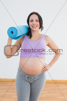 Happy pregnant woman holding exercise mat smiling at camera