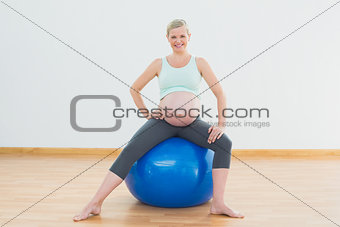 Smiling blonde pregnant woman sitting on blue exercise ball