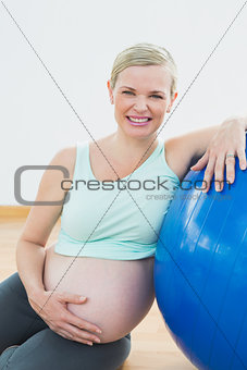 Happy pregnant woman leaning against exercise ball holding her belly