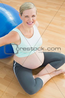 Pregnant woman sitting beside exercise ball smiling up at camera