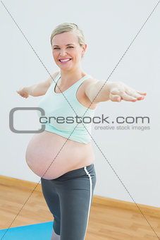 Blonde pregnant woman doing yoga on mat smiling at camera