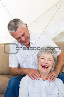 Man giving his senior wife a shoulder rub who is smiling at camera