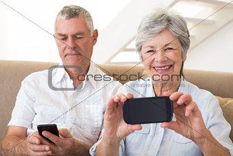 Senior couple sitting on couch using their smartphones