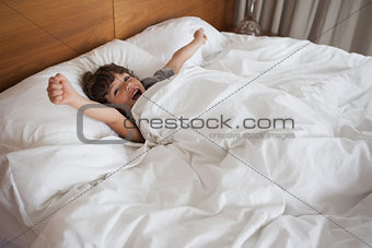 Boy yawning while stretching arms in bed