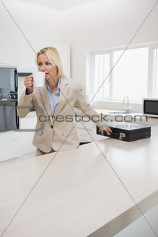 Well dressed woman drinking coffee while holding briefcase in kitchen