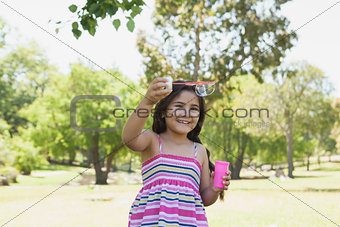 Cheerful girl blowing soap bubbles at park