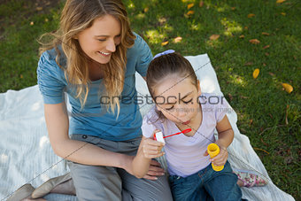 Mother with her daughter blowing soap bubbles at park