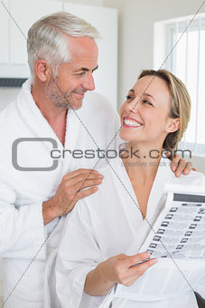 Happy couple reading newspaper together in bathrobes