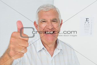 Smiling senior man gesturing thumbs up with eye chart in background