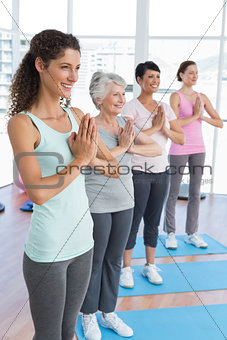 Class standing in namaste pose at yoga class