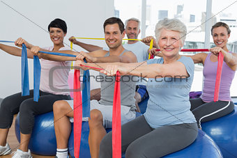 Class holding out exercise belts while sitting on fitness balls