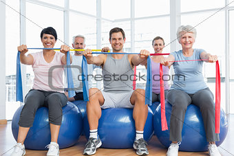 Class holding exercise belts while sitting on fitness balls