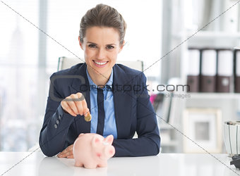 Happy business woman putting coin into piggy bank