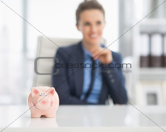 Closeup on piggy bank on table and happy business woman in backg