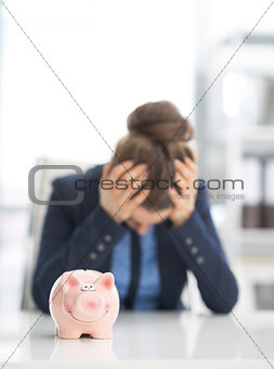 Closeup on piggy bank on table and stressed business woman in ba