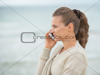 Young woman talking cell phone on cold beach
