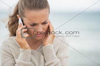Concerned young woman talking cell phone on cold beach