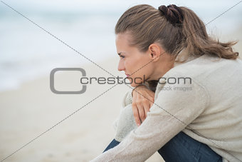 Calm young woman sitting on cold beach and looking into distance