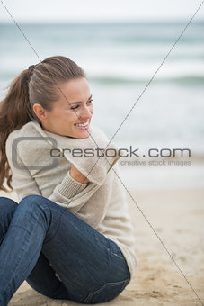Happy young woman sitting on cold beach and looking into distanc