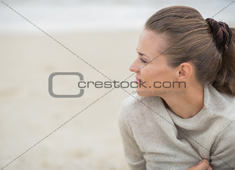 Calm woman sitting on cold beach and looking into distance
