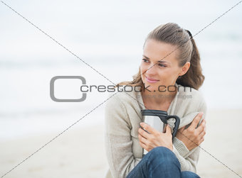 Relaxed woman sitting on cold beach with cup of hot beverage