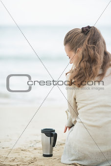 Woman sitting on cold beach with cup of hot beverage