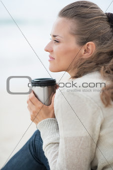 Calm woman sitting on cold beach with cup of hot beverage