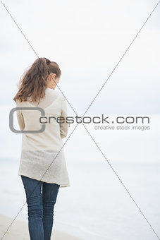 Young woman walking on cold beach. rear view
