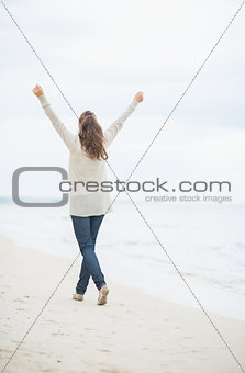 Full length portrait of young woman walking on cold beach. rear 