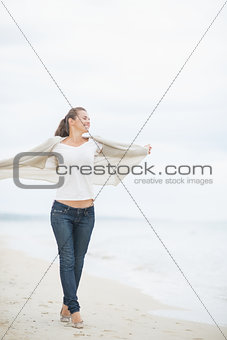 Full length portrait of young woman walking on cold beach and re