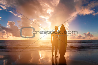 surfing man standing on a beach with sunset background