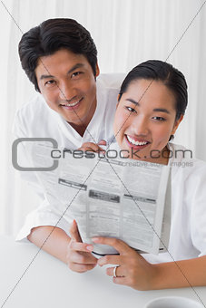 Couple in bathrobes reading newspaper together in the morning