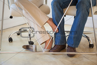 Casual businesswoman playing footsie with colleague under desk