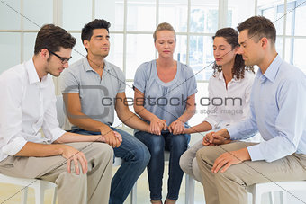 Group therapy in session sitting in a circle holding hands