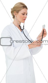 Blonde doctor in lab coat listening with stethoscope