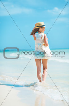 Young woman in hat with bag walking at seaside. rear view