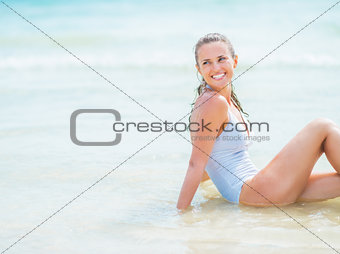 Happy young woman in swimsuit sitting on sea coast and looking o