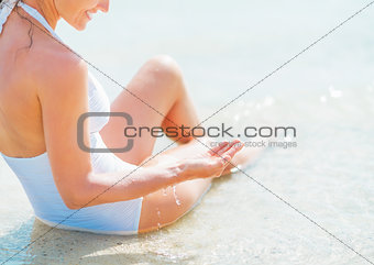 Closeup on young woman in swimsuit sitting on sea shore and play