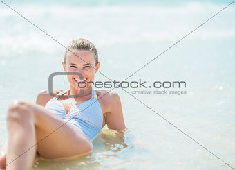 Happy young woman in swimsuit laying in water at seaside