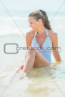 Happy young woman in swimsuit sitting in water at seaside