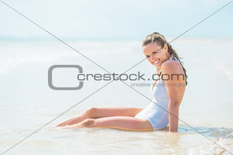 Smiling young woman in swimsuit sitting in water at seaside
