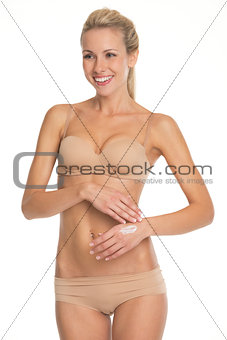 Smiling young woman in lingerie applying creme on hand
