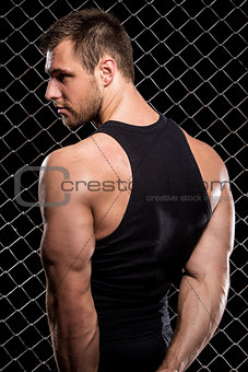 Guy showing his muscles on fence background