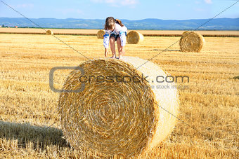 small rural girl on the straw after harvest field with straw bal