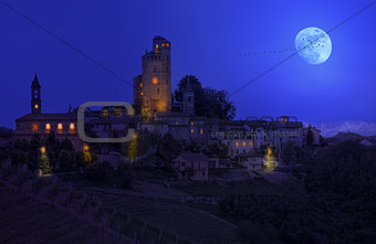 Small town on the hill under the sky with full moon at night in Piedmont, Northern Italy.